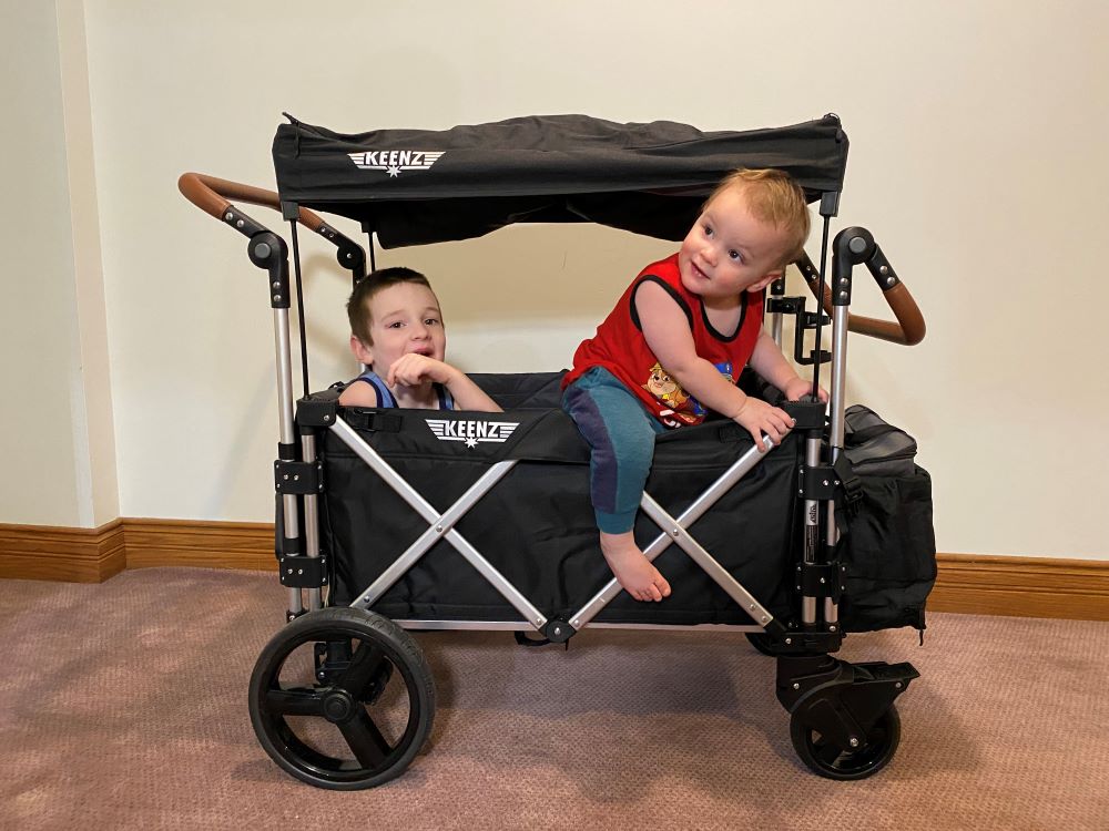 keenz 7s stroller wagon, two kids inside, toddler crawling out