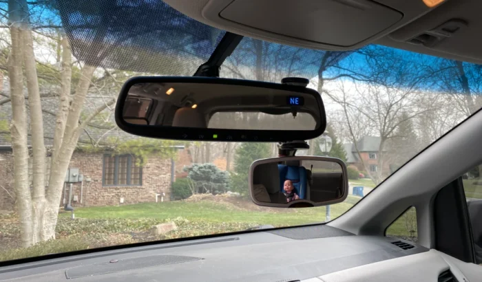 Diono see me too mirror attached to vehicle's rear-view mirror showing a kid in a forward facing car seat in the reflection