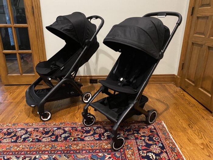 the bugaboo butterfly stroller sitting next to the joolz are on its right. Both strollers are black.
