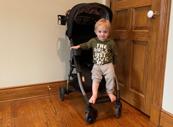 grandson standing on footrest of the zoe tour+ luxe stroller