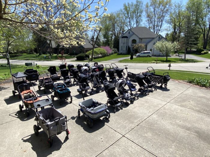 30+ different stroller and stroller wagon models collected by kid travel and arranged in rows on the driveway